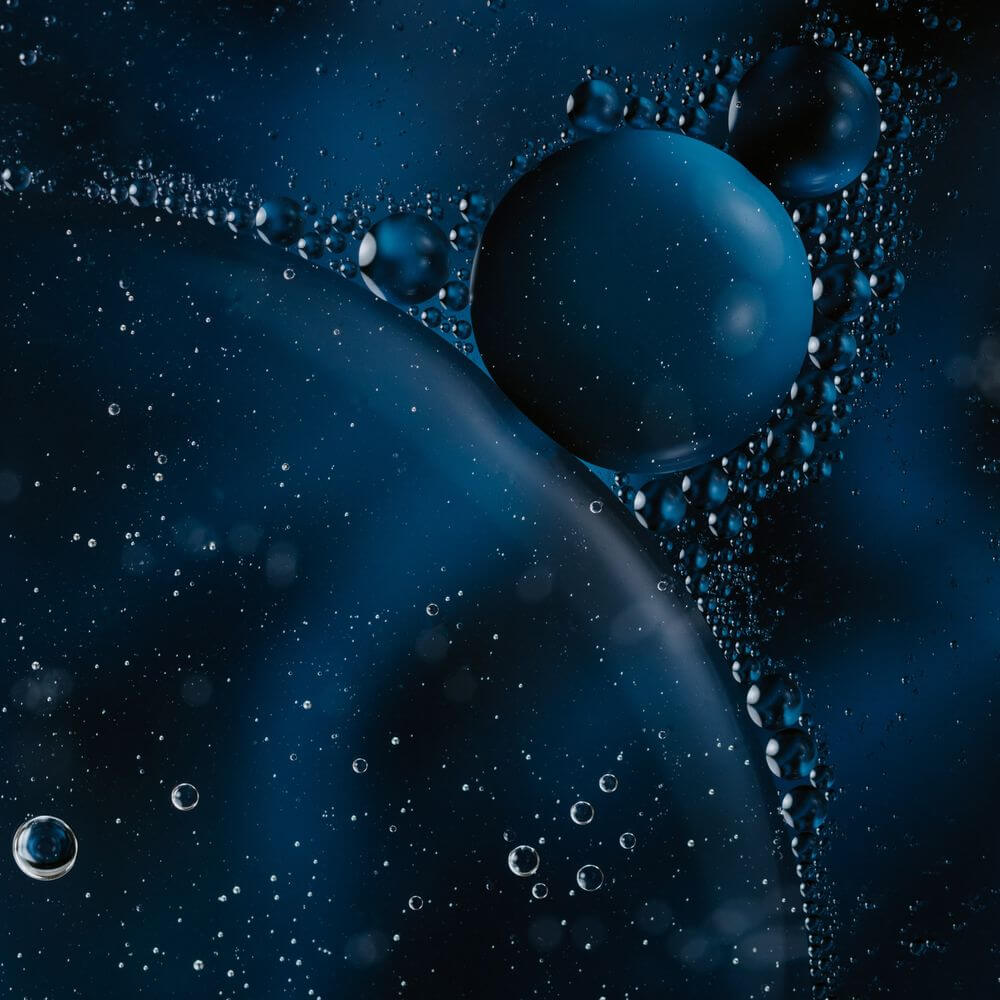 Abstract blue spheres and water droplets flowing against a dark blue background, symbolizing innovation and funding.