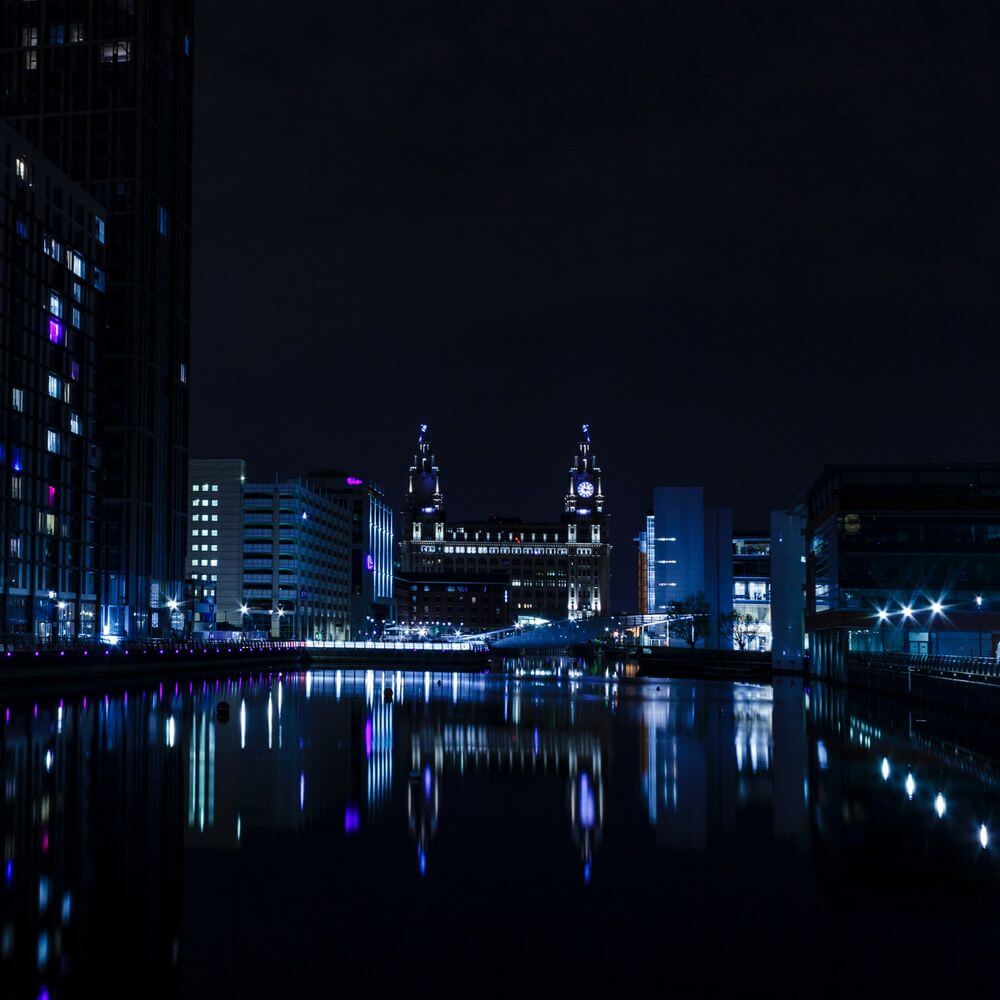 Liverpool waterfront at night with illuminated historic buildings and clock tower reflected in calm water