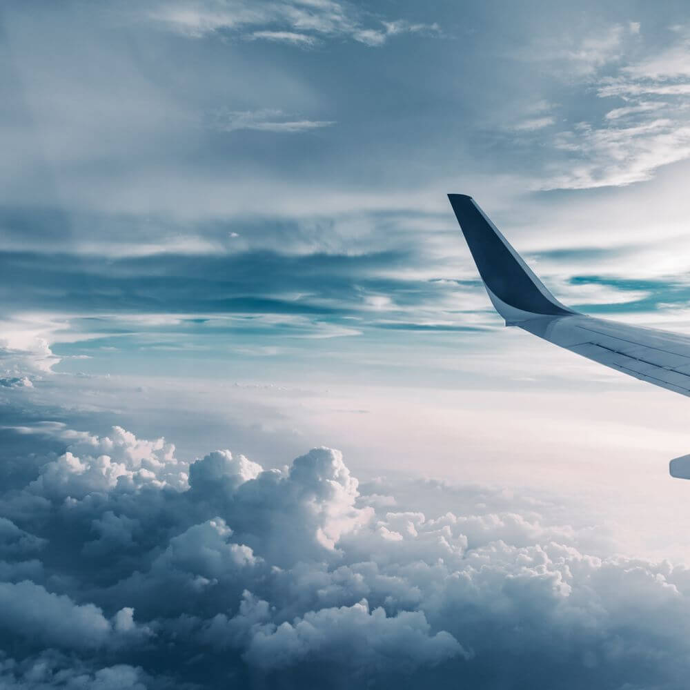 Airplane wing in flight above clouds, representing aviation industry partnership for green hydrogen development.