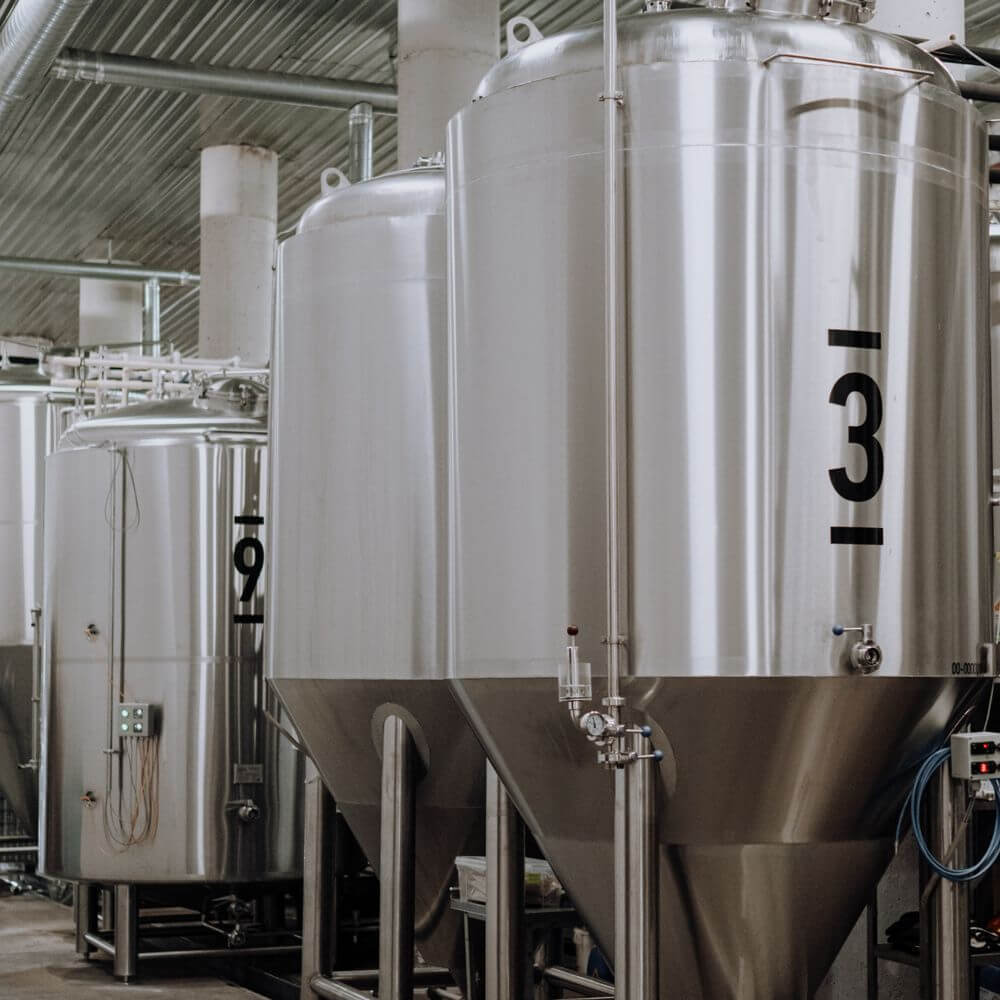 Industrial stainless steel storage tanks numbered 9 and 3 in a factory facility with corrugated metal roof and piping syst...