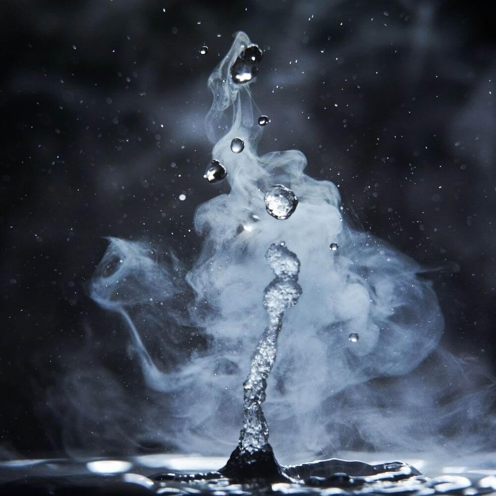 Hydrogen molecule visualization with water droplets and dynamic splashing effect against dark background.