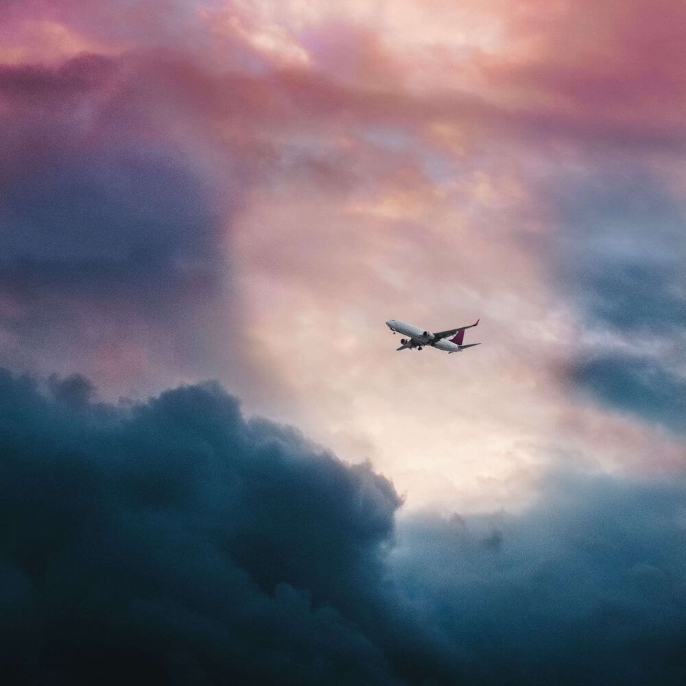 Commercial aircraft flying through dramatic pink and blue cloudy sky at sunset or sunrise.
