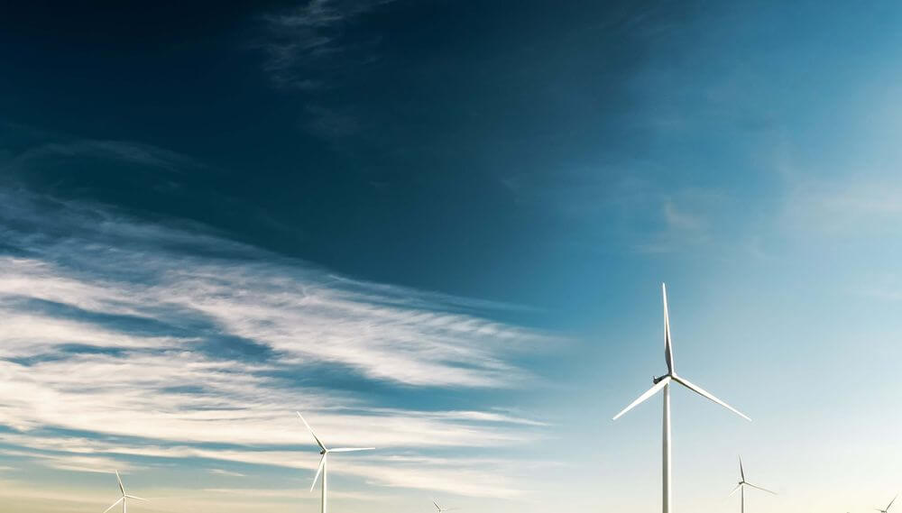 Wind turbines against a blue sky with white clouds, symbolizing renewable energy and green hydrogen technology partnership.