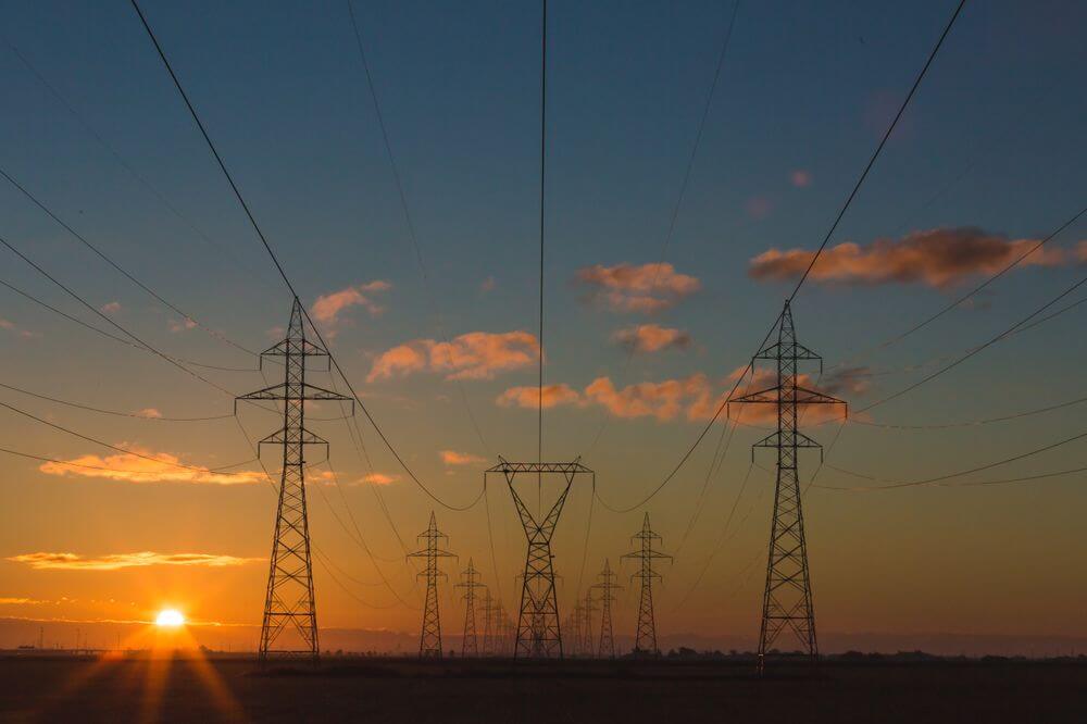 Electricity transmission towers and power lines at sunset, symbolizing energy infrastructure and investment.