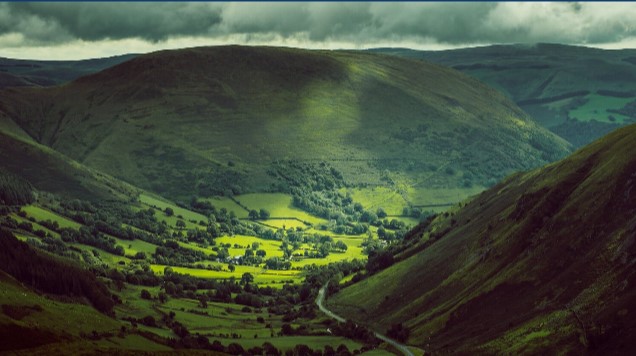Aerial view of Samlesbury valley with rolling green hills, farmland, and winding river under cloudy sky.