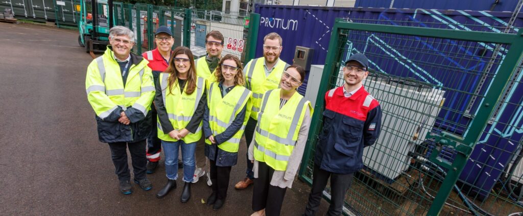 Group photo of staff and visitors wearing safety vests at Protium's green hydrogen facility in Baglan, Wales, standing bef...