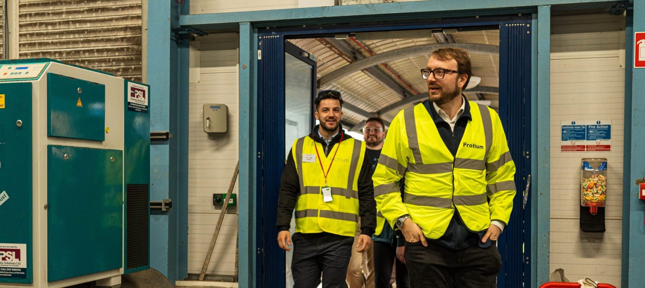 Protium team members wearing yellow safety vests inside green hydrogen production facility during anniversary celebration.