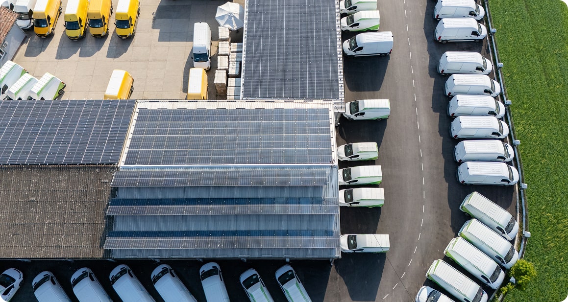 Aerial view of transport facility with solar panels, electric vehicles charging, and parked delivery trucks.