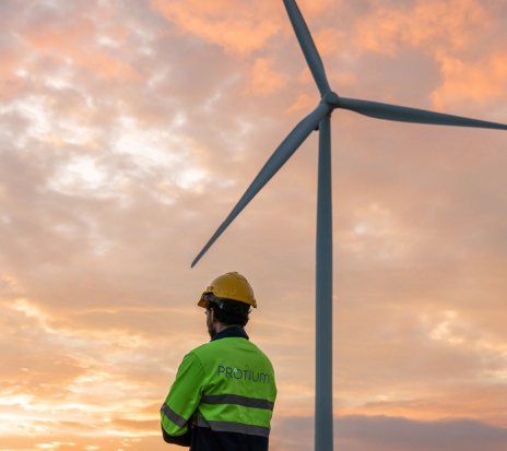 Worker in safety gear viewing wind turbine at sunset, representing renewable energy commercial development.