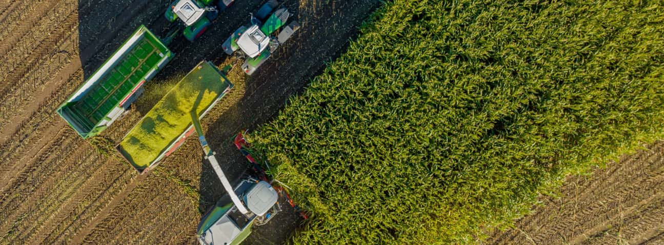 Aerial view of agricultural equipment and vehicles on farmland with green crop fields and dirt roads.