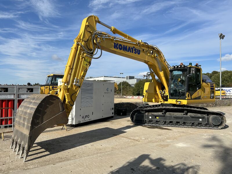 Yellow Komatsu excavator positioned next to white off-grid power generator unit on construction site