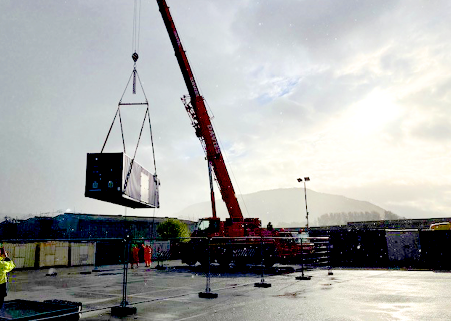 Industrial crane lifting a hydrogen distribution module at a UK production facility with mountains visible in the background.