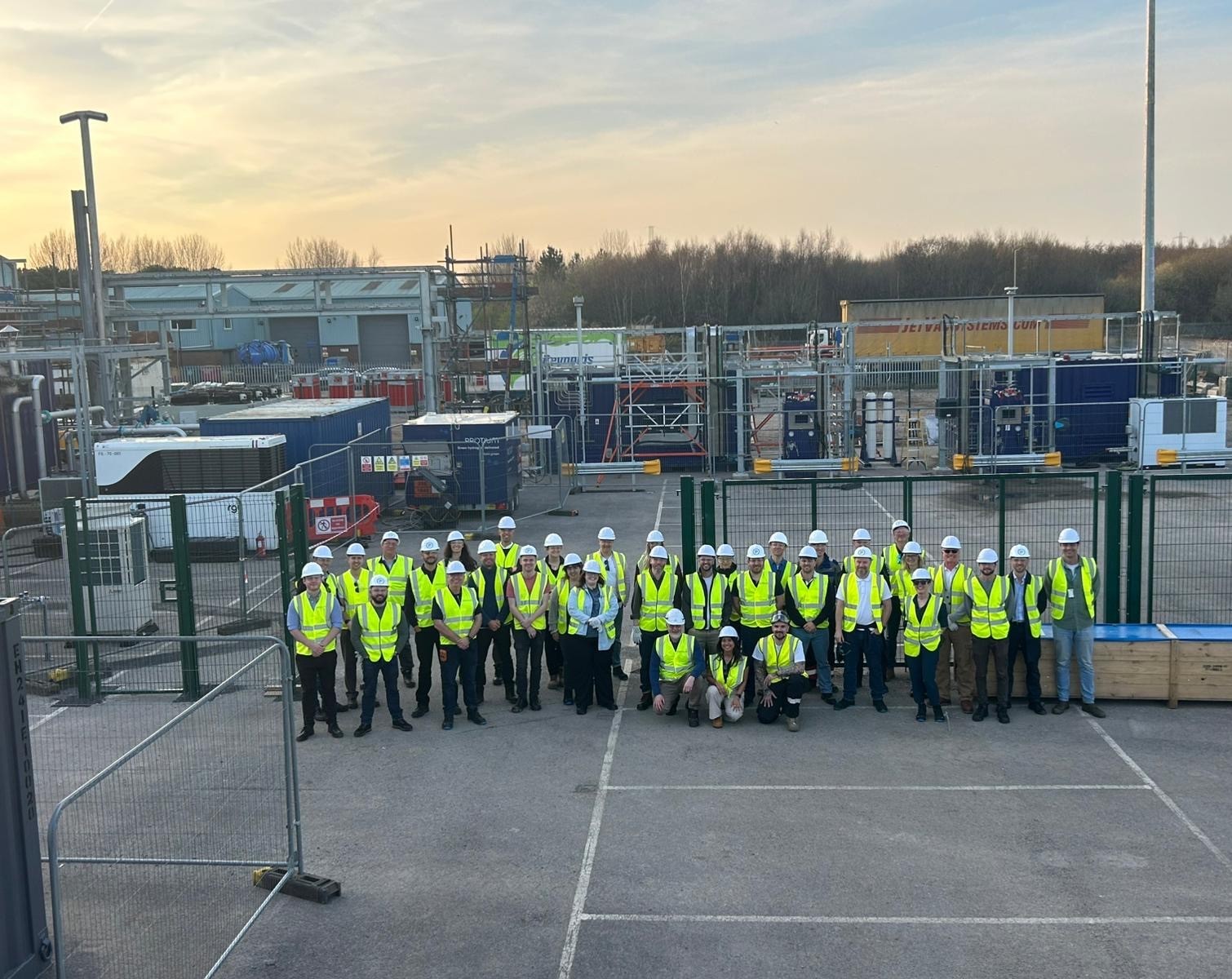 Team group photo at Pioneer 2 construction site with workers in safety vests and hard hats standing in front of industrial...